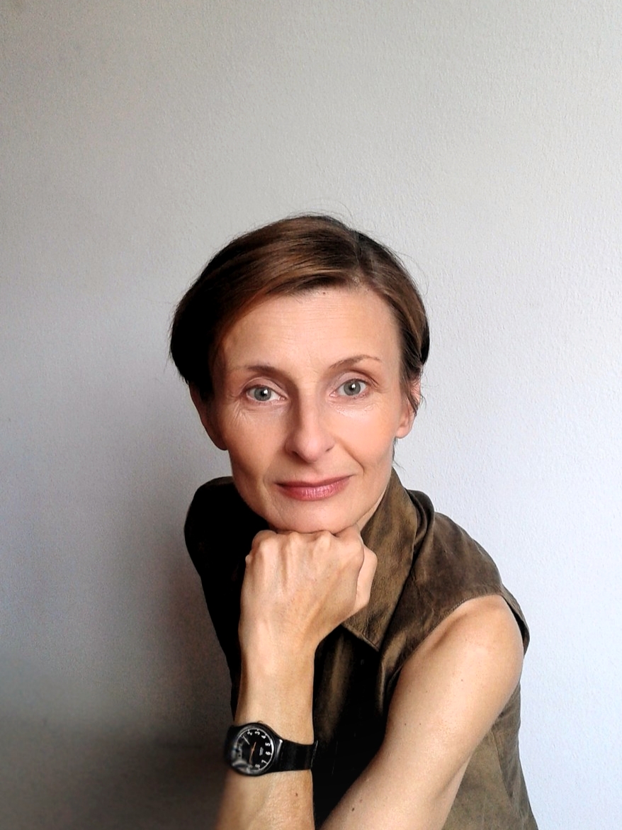 Maja Vujovic in a sleeveless brown shirt, seated, her chin resting on her fist, looks straight into the camera, smiling.